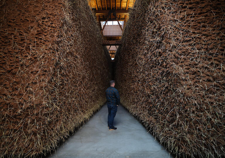 A man stands in between two walls of mud in an art installation. 