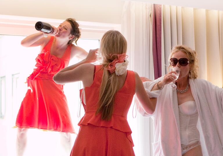 A bride and her two bridesmaids down prosecco in a hotel room.