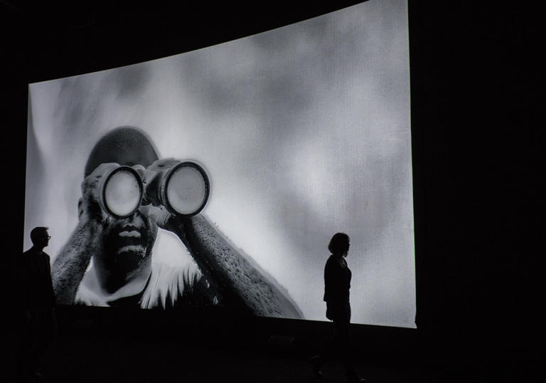 Photo of figure watching screen projections by Richard Mosse Incoming