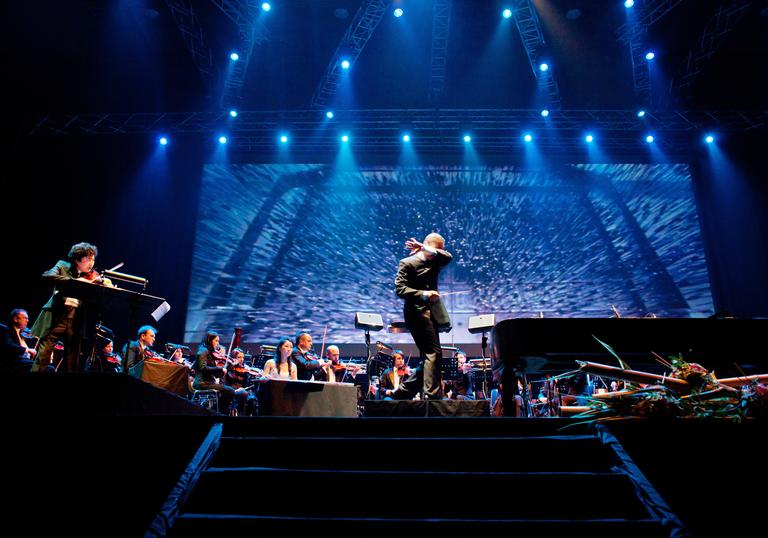 Tan Dun conducting an orchestra while the film plays behind them