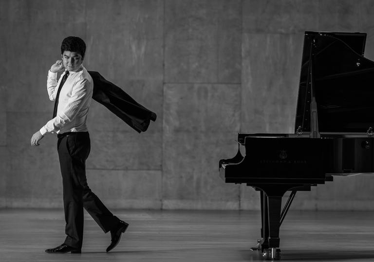 A black & white picture of Behzod Abduraimov walking away from a piano