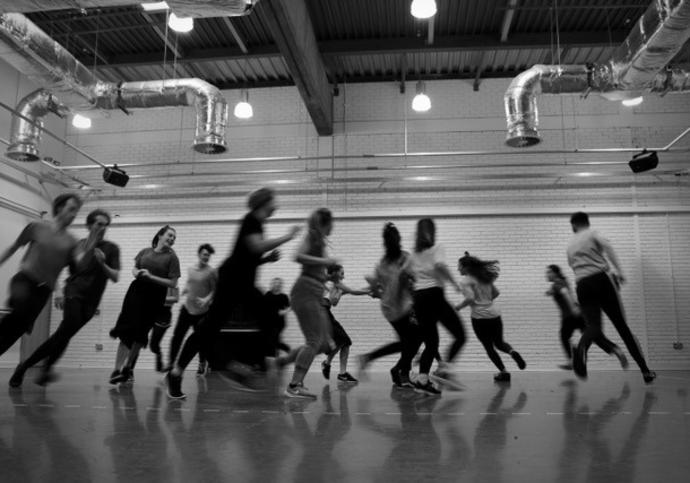 Black and White image of children running in a circle in a rehearsal room