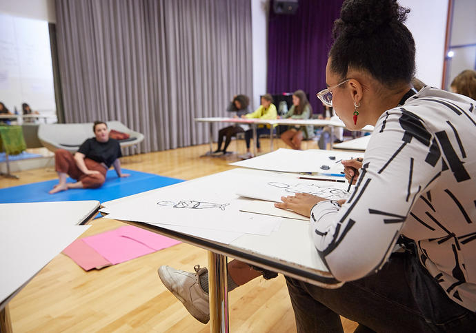 a women sitting on the floor, while people sit around on tables and draw