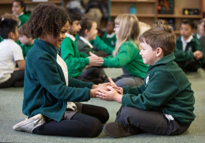 Photo of two school children sitting down facing one another and hold hands