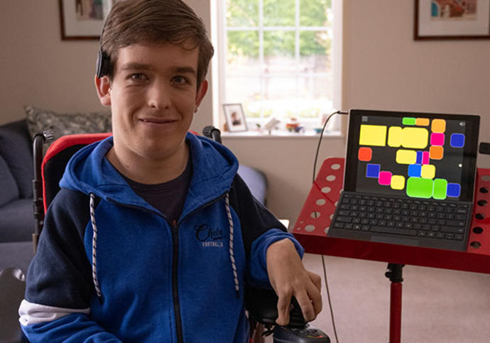 Young man in wheelchair sits next to a screen, a clarion instrument.