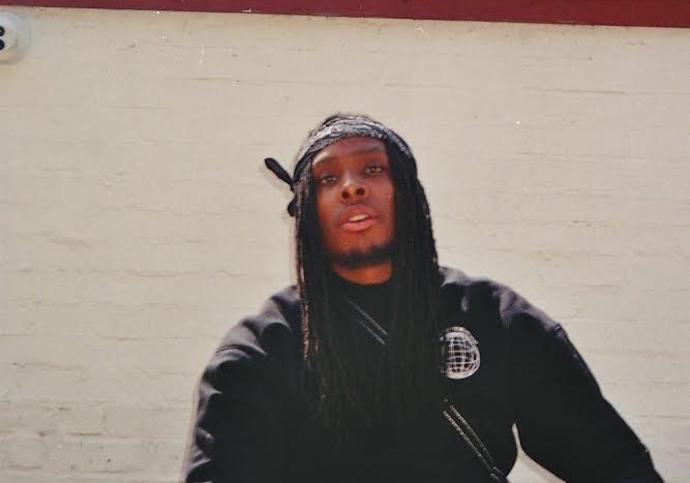 photograph of black make wearing all black with locs under a hat