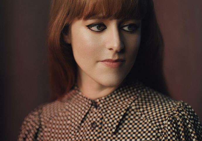 Hannah is standing in front of a deep purple background in a brown and white polka dot blouse