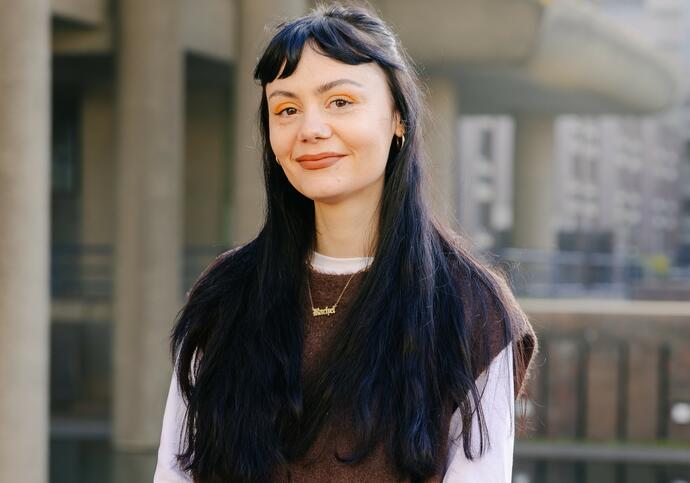 Image of Rachel smiling, wearing brown vest over white top, long dark hair