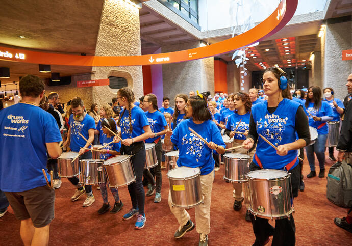 Group of people in blue shirts participating in drumming workshop