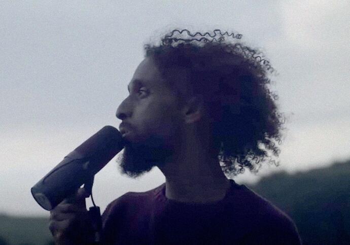 Side profile photograph of artist Faisal. He has curly hair and speaking into a microphone.