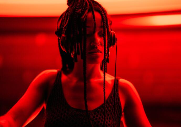 Image of DJ she is wearing headphones, and standing in a red lit room