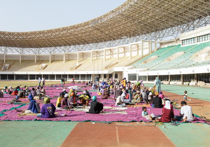 people sit inside a stadium sewing fabric for ibrahim mahama's purple hibiscus