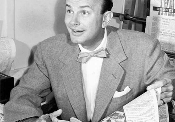 Black and white image of Jack Paar in a suit reading a newspaper on a table
