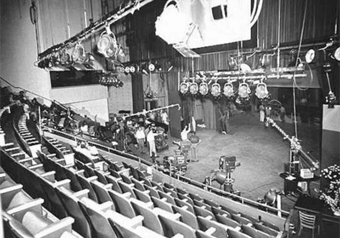 Image of a concert hall where there are rows of seats facing a stage with multiple lights hanging above the stage