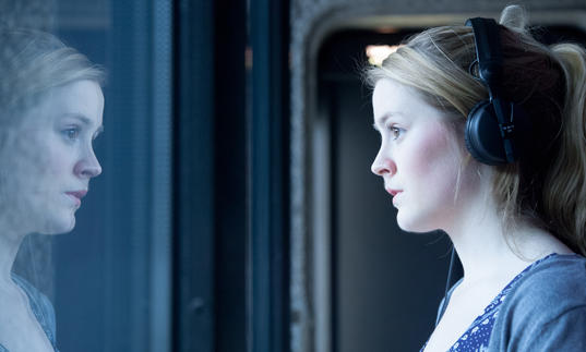 Photo of woman wearing headphones looking out of a window