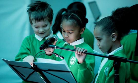 Photo of three young children by a microphone looking at sheet music