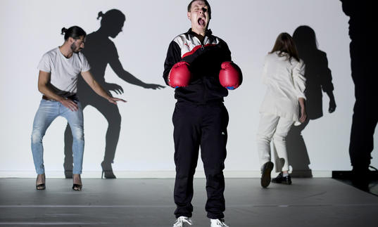 three people on a stage, one wears boxing gloves and screams