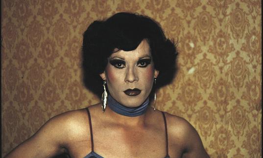 Gazing directly into the camera, Paz Errazuriz’s arresting photograph of Pilar, a cross-dresser working in an underground brothel in Chile during the 1980s.
