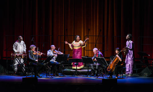 Kronos Quartet performing with Trio Da Kali on a stage with a red curtain backdrop