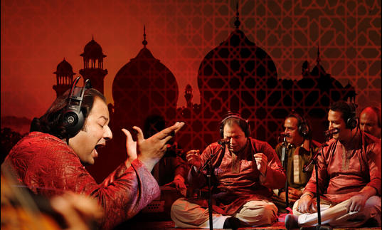 Rizwan-Muazzam Qawwali perform tradition instruments and sing seated with a backdrop of a mosque