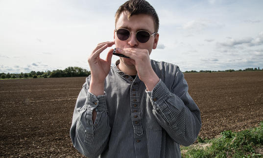 Oliver Cross playing his harmonica in a field