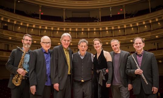 The Philip Glass Ensemble with Philip Glass pose for a photo in a concert hall