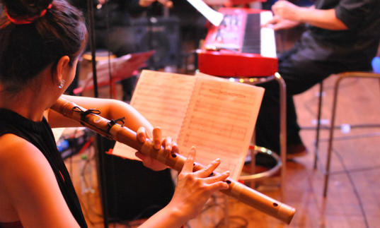 A woman playing flute and reading a piece of music