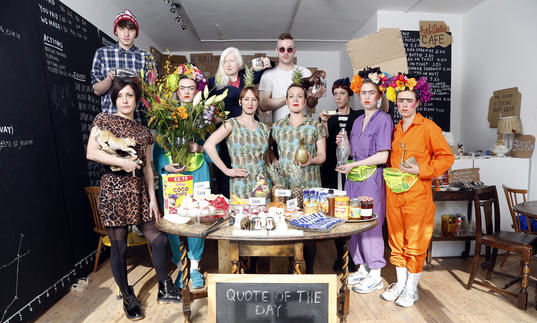 A group of people standing in a huddle around a circle table, wearing elaborate oufits.