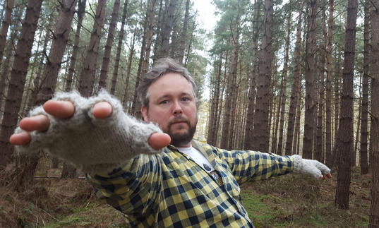 A man standing in the woods with an outstretched towards the camera