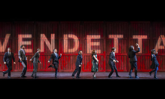 Ten people stand in various poses in front of a red wall which spells out 'vendetta'