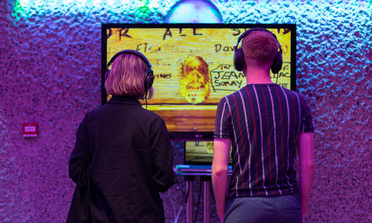 A couple with headphones on looking at a screen