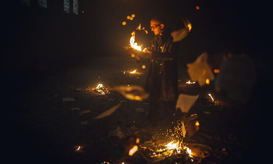 paper falls from ceiling , man burns paper, fire pit on the ground 