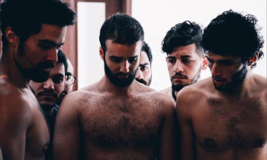 a group of topless men stand looking at the floor