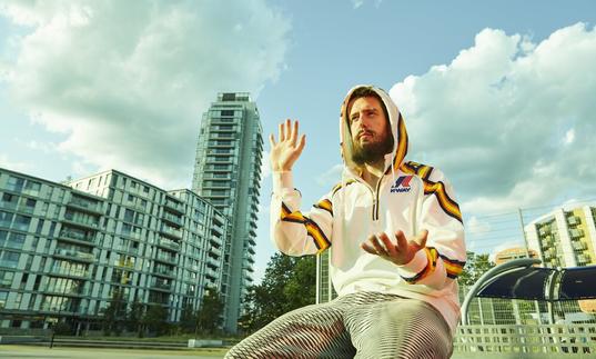 Danalogue sitting amongst glass buildings, gesturing with his hands