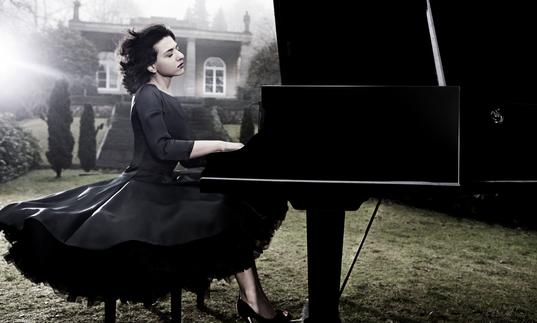 An ethereal image of Khatia in a stately garden with wind in her hair, expertly playing the piano with great emotion