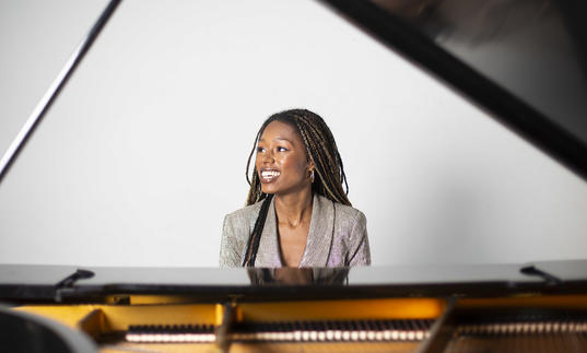 Am image of Isata sitting by the piano and smiling
