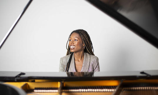 Am image of Isata sitting by the piano and smiling 