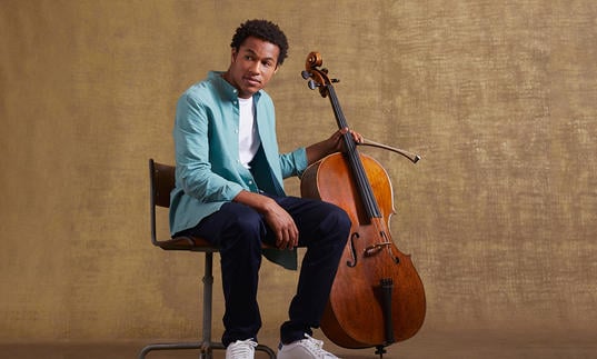 Sheku sitting on a chair holding his cello 