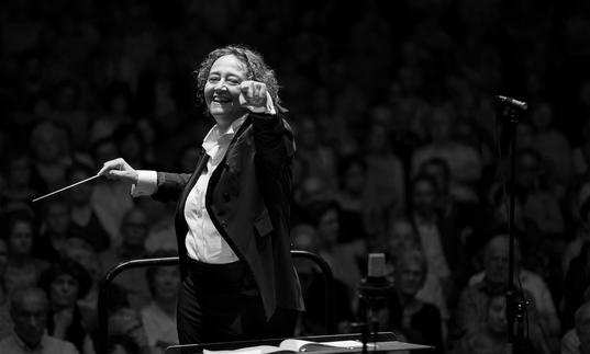 An image of Nathalie pointing at the camera joyfully whilst conducting in a recent concert