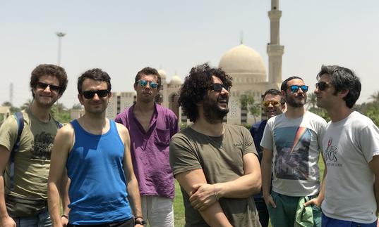 Sofiane Saidi & Mazalda standing in front of a mosque, wearing sunglasses in the sunshine