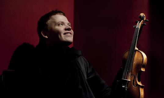 Pekka smiling joyfully as he gazes into the middle distance, violin in hand