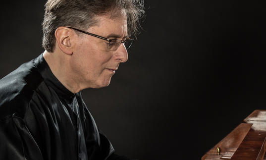 Robert Levin playing the piano, wearing a flowing black silk shirt 