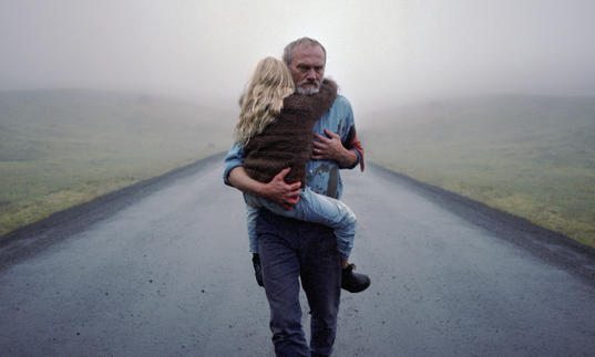 A man carrying a young girl along a deserted road