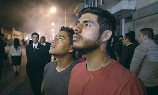 two men are in a busy street at night looking up towards the sky