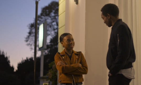 a man and a woman stand outside a building talking to each other at dusk