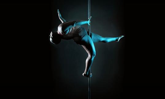 a fat black dances on a pole in darkness, lit by a blue light