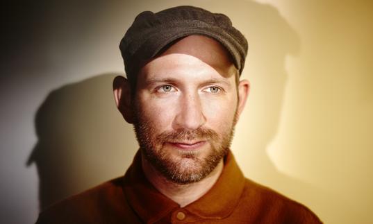 photo of Matthew Halsall wearing a cap and shirt against a plain backgound, being lit from multiple sources to create shadows