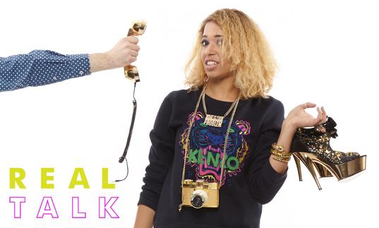 Paula Varjack holding high heeled shoes and looking bemused as a phone is pointed at her