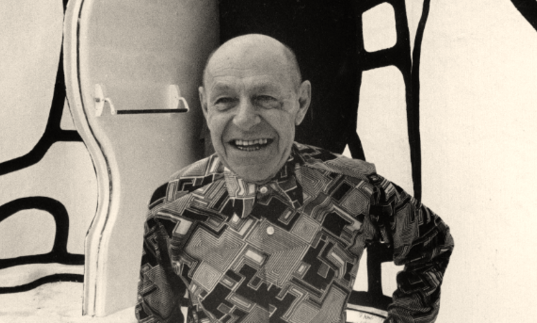 black and white photo of jean dubuffet smiling against some sort of wall with giant black lines