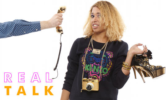 Paula Varjack holding high heeled shoes and looking bemused as a phone is pointed at her